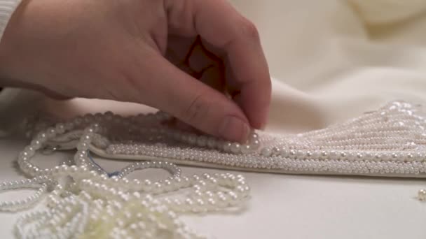 Zbliżenie dłoni kobiecej pasujące trzy ciągi perła do zroszony koronki na sukni ślubnej i wybrania najlepszego z nich ozdobić — Wideo stockowe