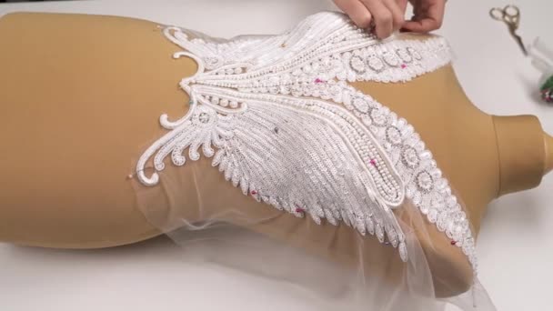 Top view of the sequined and beaded lace pinned to the veil cloth on the mannequin. Female hands are adjusting and stretching the lace. — Stock Video