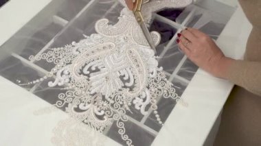 Büyük makas ve daha sonra daha küçük makas ile pullu ve boncuklu dantel bir tasarımcı kesmek bir üstten görünüm