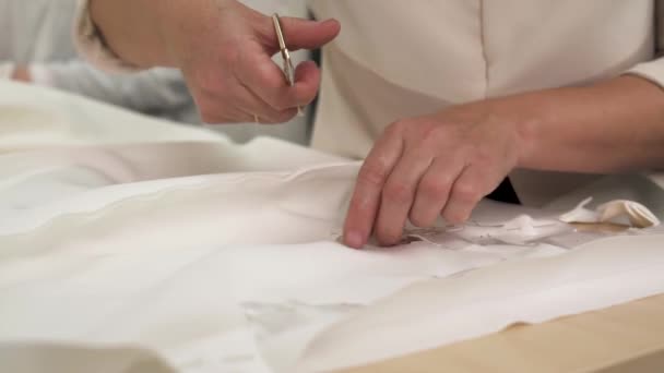 Жіночі руки тримають ножиці і вирізають тканину, щоб слідувати за формою і візерунком. Весільна сукня — стокове відео