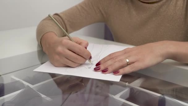 Крупним планом руки дизайнера продовжують працювати над ескізом весільної сукні і малювати її олівцем — стокове відео