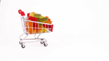 Alışveriş sepeti tatlı sakızlı şeker şeklinde ayı ile ileri hareket ediyor. Beyaz arka plan üzerinde izole. Yakın çekim. Makro.