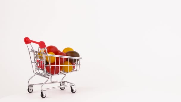 Moving supermarket trolley packed with multicolored grape tomatoes pile. Isolated on the white background. Close-up. Macro. — Stock Video