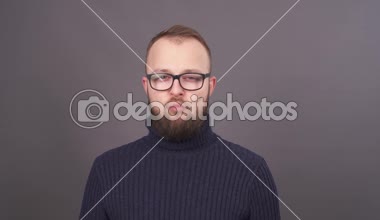 Gözlüklü, sakallı genç bir beyaz adam portresi yakın çekim kamera diş etleri gösterir. Ağız içine koyar ve çiğnemek ve ağzını şapırdatarak yemek başlar. Gri arka plan üzerinde izole.