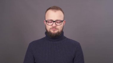 Yakın çekim portre baş ağrısı acı bardaklarda sakallı genç bir beyaz adam. Kafasını dokunmadan aşağı, bakar ve tapınaklar kendi kendine masaj yapar. Gri arka plan üzerinde izole.