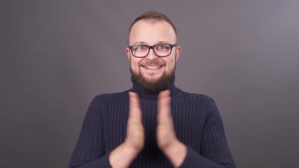 Gros plan portrait d'un jeune homme caucasien barbu dans des lunettes battant des mains. Isolé sur fond gris . — Video