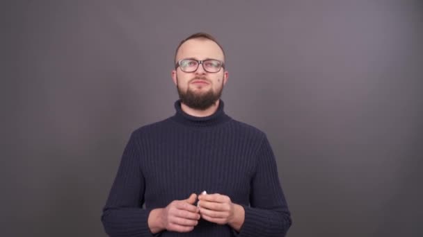 Porträtt av en ung skäggig man i glasögon som försöker sluta röka. Isolerad på grå bakgrund. — Stockvideo
