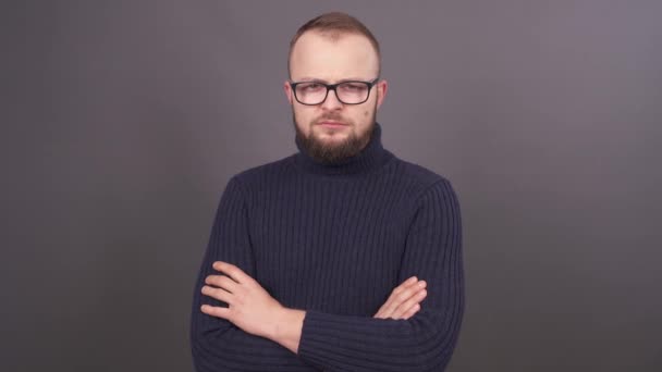 Portrait of the surprised young bearded Caucasian male with brown hair looking at camera and pulls the neck on a grey background. — Stock Video