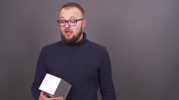 Retrato de cerca de un joven mocoso barbudo con gafas sonándose la nariz en servilletas. Aislado sobre fondo gris . — Vídeo de stock