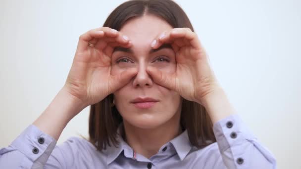 Un retrato de una guapa morena sosteniendo sus manos imitando binocular y mirando a la cámara con ojos entrecerrados — Vídeos de Stock