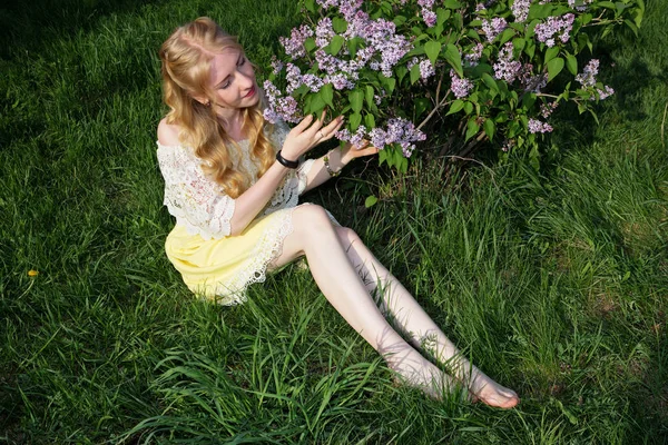 緑の草の上に座って ライラックの花に見とれながら裸足少女 — ストック写真