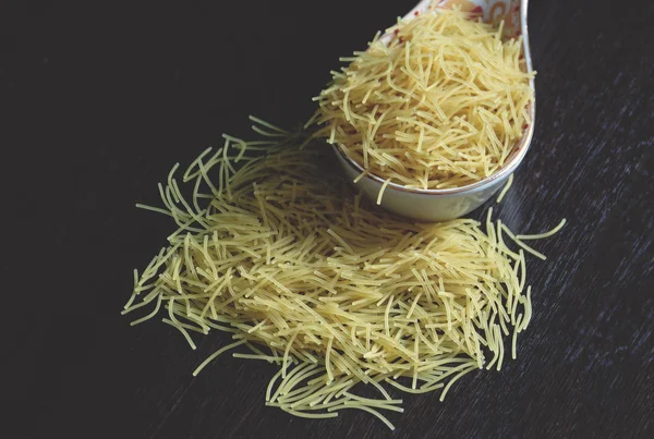 Koyu ahşap masa ve bir kaşık toplanan makarna parçası üzerinde dağınık makarna parçası.