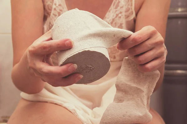 Woman sitting on the toilet with toilet paper.