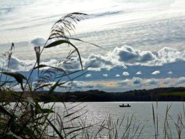Gün batımında güzel bir gölde balıkçı teknesi ve iki balıkçı ile sakin bir manzara.