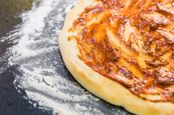 Preparing pizza, close-up of pizza dough with tomato sauce.