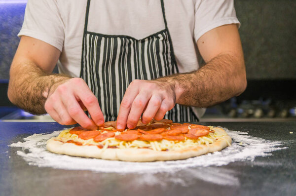 Man preparing pepperoni pizza on black granite table