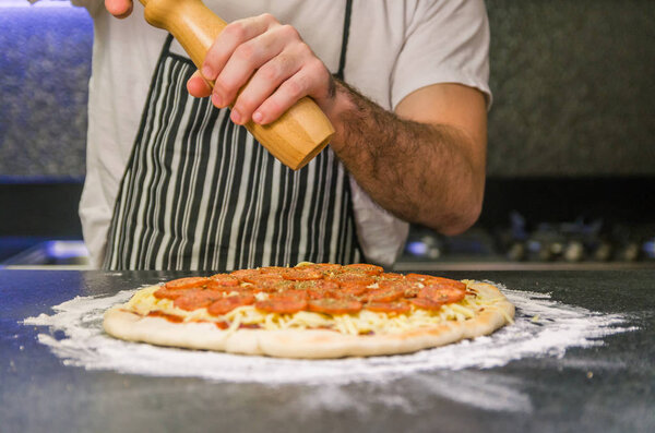 Man preparing pepperoni pizza on black granite table