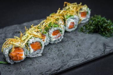 Suşi, geleneksel Japon mutfağı. Süslü tabakta nefis Uramaki, siyah arka plan.
