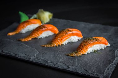 Mükemmel suşi, geleneksel Japon mutfağı. Süslü tabakta lezzetli somon kiguiri, siyah arka plan..