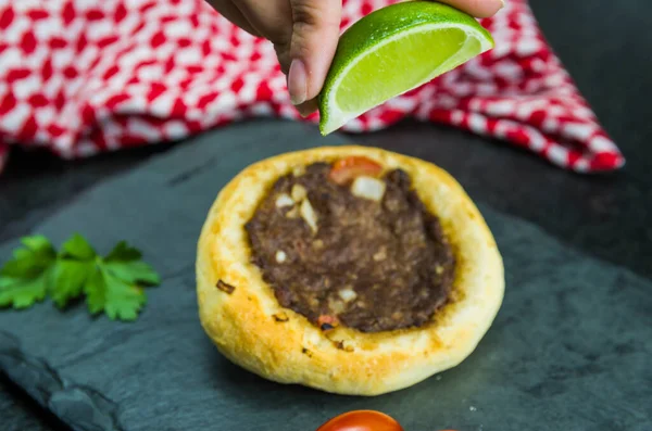 Delicious Lebanese (Arabic) food, squeezing lemon into legitimate sfihas on a black granite background with tomatoes, lemons with Keffiyeh in the background.