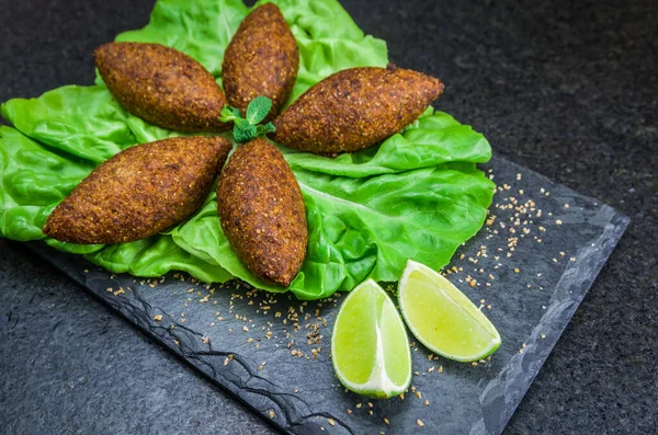 Delicious Lebanese (Arabic) food, kibbeh (kibe) on black slate stone and granite background.