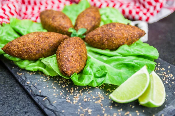 Delicious Lebanese (Arabic) food, kibbeh (kibe) with sauces and lemon on black slate stone and granite background with traditional keffyeh.