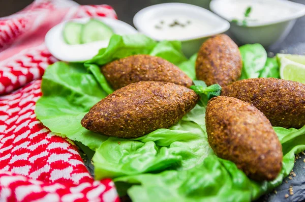 Delicious Lebanese (Arabic) food, kibbeh (kibe) with sauces and lemon on black slate stone and granite background with traditional keffyeh.