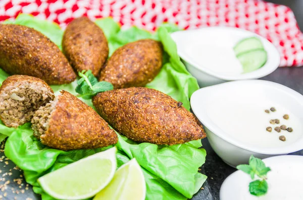 Delicious Lebanese (Arabic) food, kibbeh (kibe) with sauces and lemon on black slate stone and granite background with traditional keffyeh.