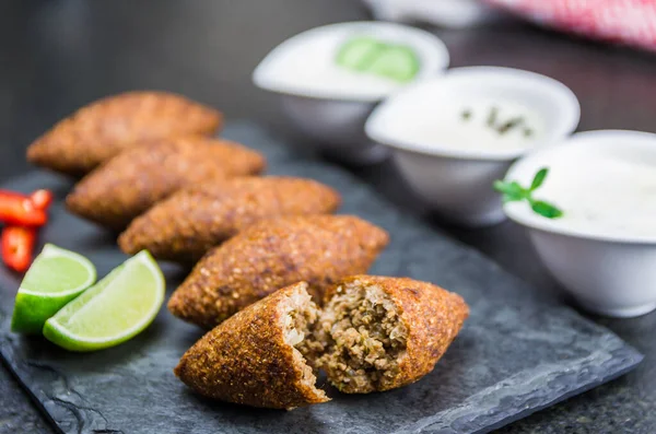 Delicious Lebanese (Arabic) food, kibbeh (kibe) on black slate stone and granite background.