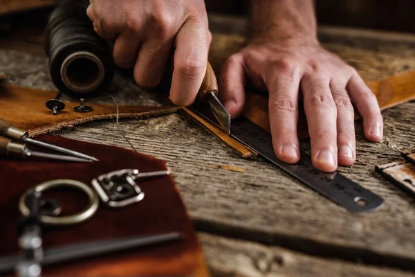 Close up of a shoemaker or artisan worker hands. Leather craft tools on old wood table. Leather craft workshop.