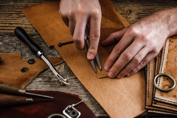 Großaufnahme der Hände eines Schuhmachers oder Handwerkers. Handwerkzeuge aus Leder auf altem Holztisch. Werkstatt für Lederhandwerk. — Stockfoto