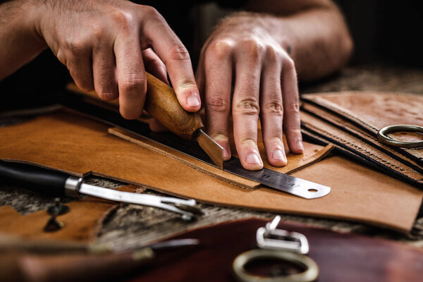 Close up of a shoemaker or artisan worker hands. Leather craft tools on old wood table. Leather craft workshop.