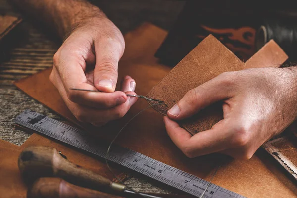 Großaufnahme der Hände eines Schuhmachers oder Handwerkers. Handwerkzeuge aus Leder auf altem Holztisch. Werkstatt für Lederhandwerk. — Stockfoto