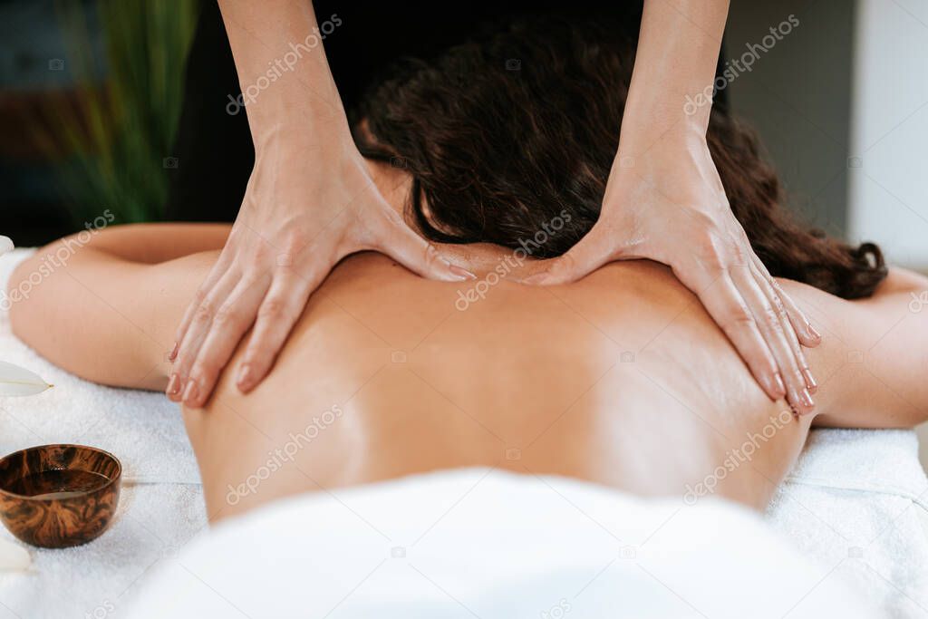 Beauty treatment concept with masseur and her patient. Masseur doing massage on woman body in the spa salon. Beautiful girl with brown curly hair and creol skin having recovery massage.