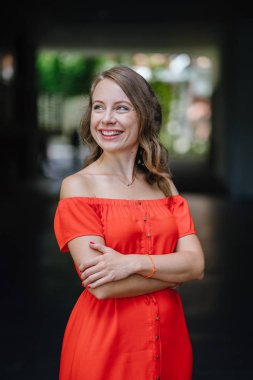 Parkta gündüz açık yürüyen bir genç, çekici beyaz kadın portresi. O güzel, hafif ve rahat Turuncu elbise giyiyordu ve şakacı gülümsüyor.