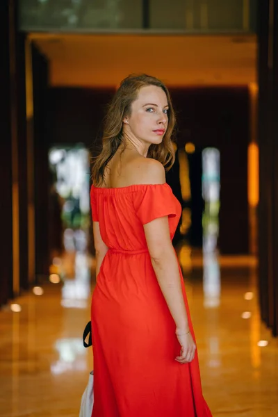 Portrait of a young, attractive European woman in an orange summer dress posing . She is blond with green eyes and is smiling confidently.