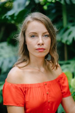 Parkta gündüz açık yürüyen bir genç, çekici beyaz kadın portresi. O güzel, hafif ve rahat Turuncu elbise giyiyordu ve şakacı gülümsüyor.