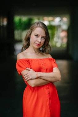 Parkta gündüz açık yürüyen bir genç, çekici beyaz kadın portresi. O güzel, hafif ve rahat Turuncu elbise giyiyordu ve şakacı gülümsüyor.