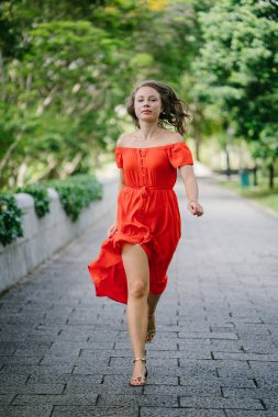 Yürüyüş / açık bir parkta bir yol boyunca gün çalışan bir genç, çekici beyaz bir kadın portresi. O güzel, hafif ve rahat Turuncu elbise giyiyordu ve şakacı gülümsüyor.