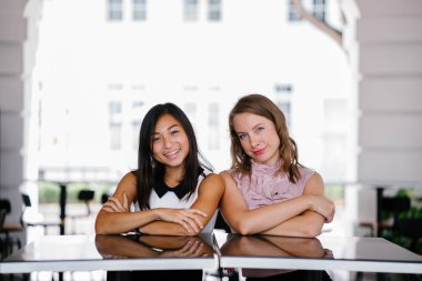 İki iş (bir Çinli Asyalı kadın ve beyaz bir kadın) farklı bir takım portresi. Onlar bir masada oturan ve gülümseyen ve kameraya gülüyor.