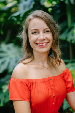 Parkta gündüz açık yürüyen bir genç, çekici beyaz kadın portresi. O güzel, hafif ve rahat Turuncu elbise giyiyordu ve şakacı gülümsüyor.