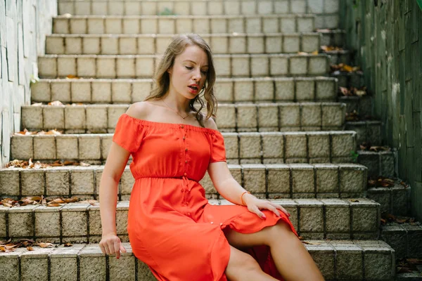 Parkta gündüz açık yürüyen bir genç, çekici beyaz kadın portresi. O güzel, hafif ve rahat Turuncu elbise giyiyordu ve şakacı gülümsüyor.