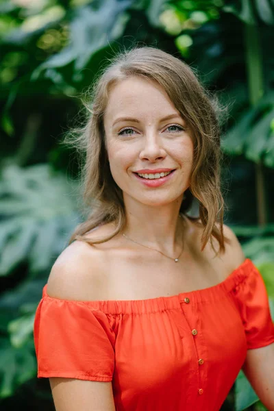 Parkta gündüz açık yürüyen bir genç, çekici beyaz kadın portresi. O güzel, hafif ve rahat Turuncu elbise giyiyordu ve şakacı gülümsüyor.