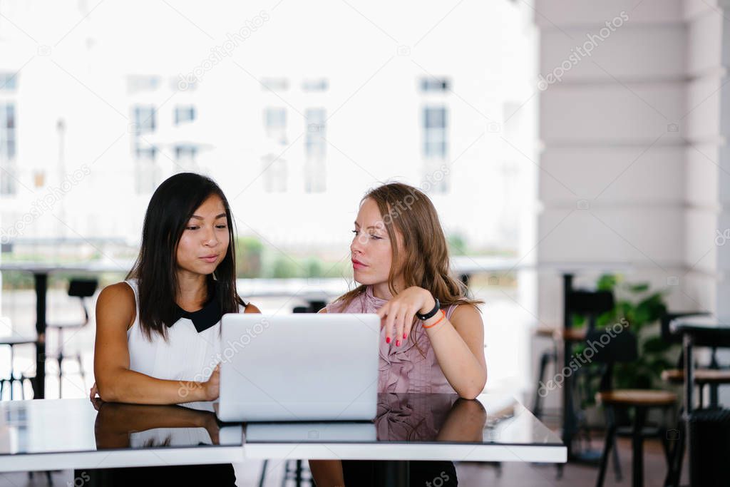 Portrait of a diverse team of two coworkers (a Chinese Asian woman and a Caucasian white woman) looking over a DCF cashflow model on a laptop computer in the day.
