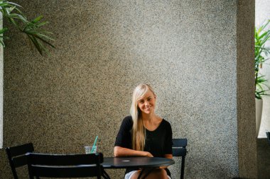  sarışın kadın bir kafede oturur ve bir içki ile gün boyunca rahatlatır genç ve güzel beyaz beyaz. Asya tropik bir şehirde değil. Gülümsüyor 