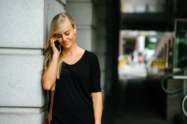 Genç ve çekici sarışın kadın turist veya exchange öğrenci telefonunu Asya'da bir sokakta gündüz kullanıyor.