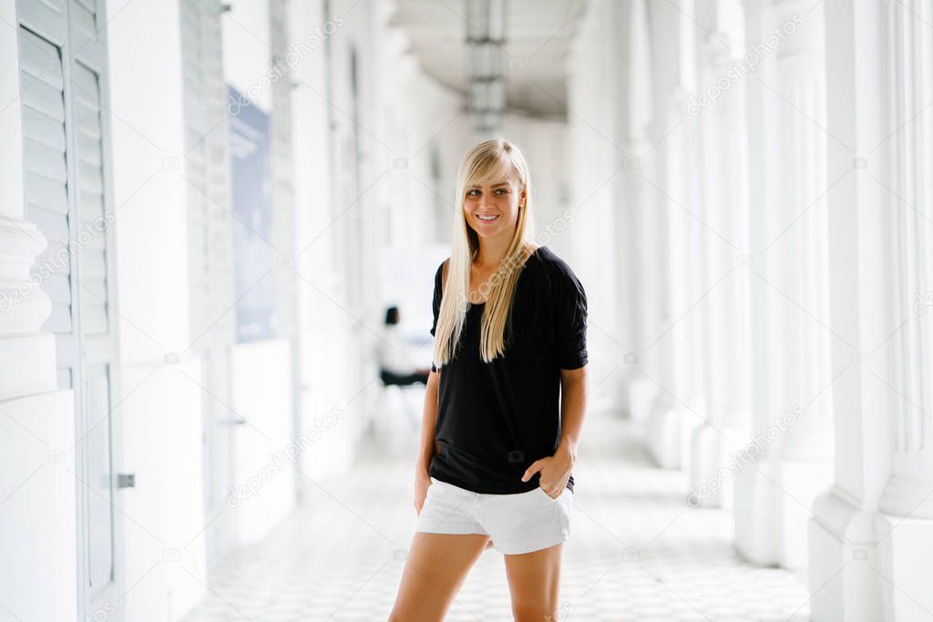 Portrait of a young, attractive blond tourist standing in a corridor of a colonial building in Asia. 