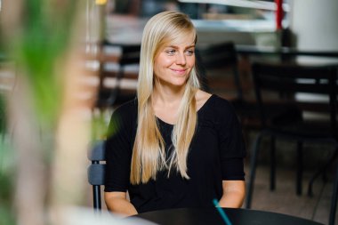  sarışın kadın bir kafede oturur ve bir içki ile gün boyunca rahatlatır genç ve güzel beyaz beyaz. Asya tropik bir şehirde değil. Gülümsüyor 