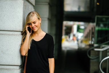 Genç ve çekici sarışın kadın turist veya exchange öğrenci telefonunu Asya'da bir sokakta gündüz kullanıyor.