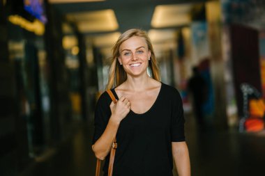 Ayakta ve gün boyunca şehrin Asya bir kampüste bir koridorda gülümseyen mavi gözlü genç ve güzel sarışın kadın öğrenci portresi. O raslantı ışık kılığına girmiş.
